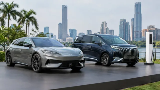 The Denza Z9 GT shooting brake and the updated Denza D9 MPV on a stage in Jakarta, with a white BYD Flash Charger unit standing beside them. AI-generated illustration.