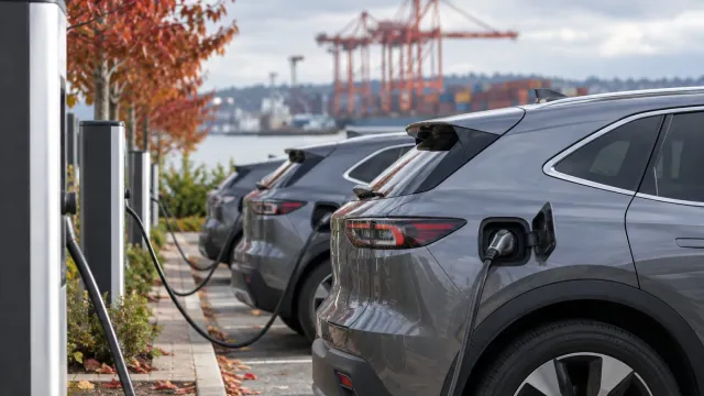 Generic plug-in hybrid SUVs parked at a charging station near a port on an overcast day. AI-generated illustration.