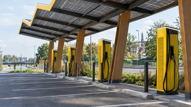 Fastned fast-charging station in Gentbrugge, Belgium, with yellow charging posts and a solar canopy above a row of parking bays. AI-generated illustration.