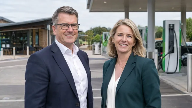 Tim Gittins, chief executive of Roadchef, and Jo Hayward, bp's vice president for mobility and convenience retail UK, standing together at a motorway service area forecourt. AI-generated illustration.