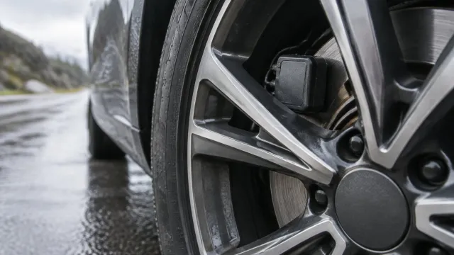 Car wheel close-up with a small device capturing tyre dust near the brake disc on a wet road. AI-generated illustration.