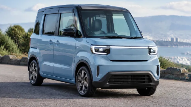 The Suzuki e-Sky kei-car EV seen from the front three-quarter angle, showing its 3,395 mm body, tall 1,625 mm roofline and short front overhang. AI-generated illustration.