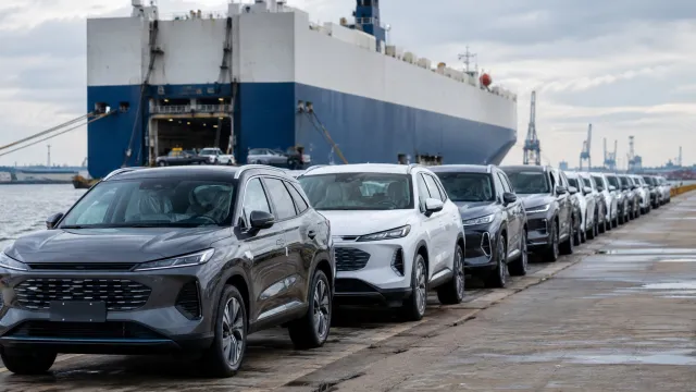 Rows of newly imported Chery cars parked on the quayside at Teesport after being unloaded from a car carrier ship. AI-generated illustration.