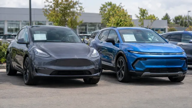 A used Tesla Model Y and a Chevrolet Equinox EV parked side by side on a dealership forecourt, with printed price sheets taped inside their windscreens. AI-generated illustration.