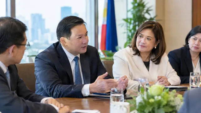 Vingroup vice chairman Nguyen Quoc Tuan seated at a table with Philippine trade secretary Cristina Roque and DTI officials during a meeting on EV manufacturing investment. AI-generated illustration.